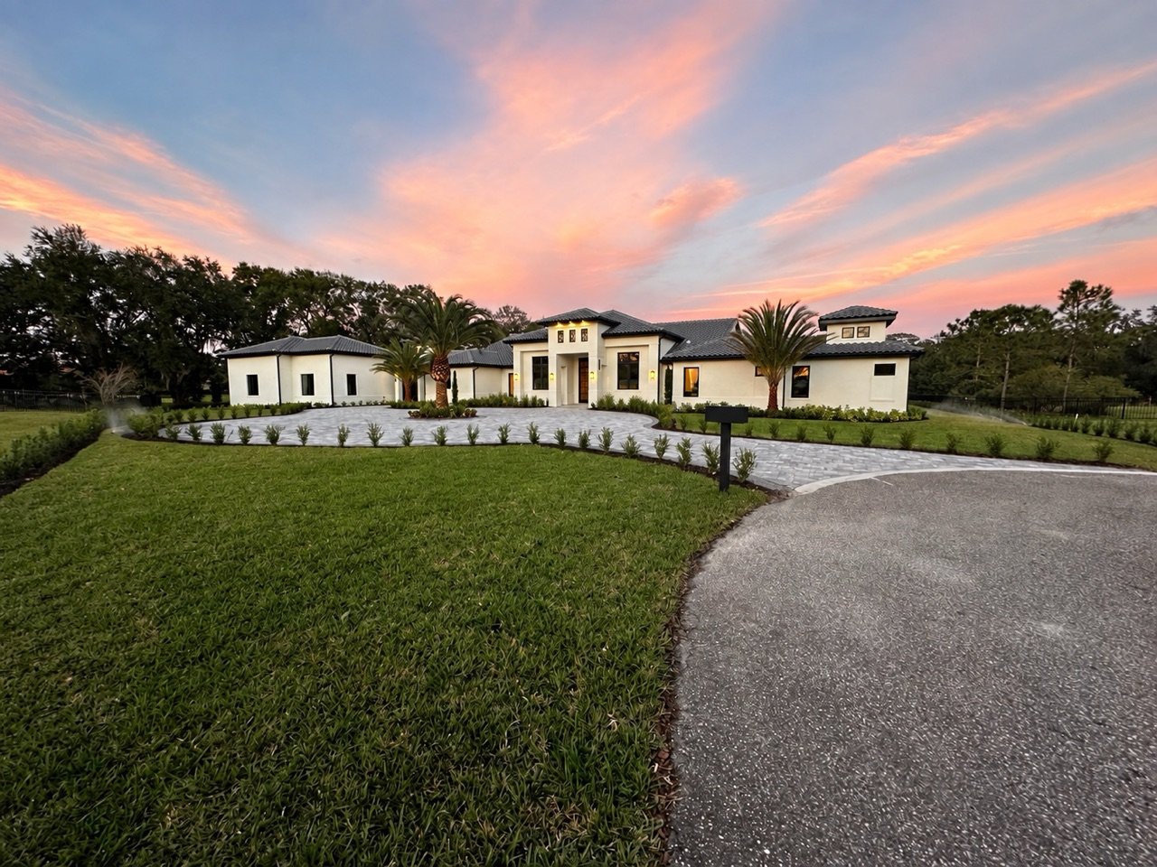 Completed custom home with a tiled roof, central entry, palm trees, and a circular driveway at sunset