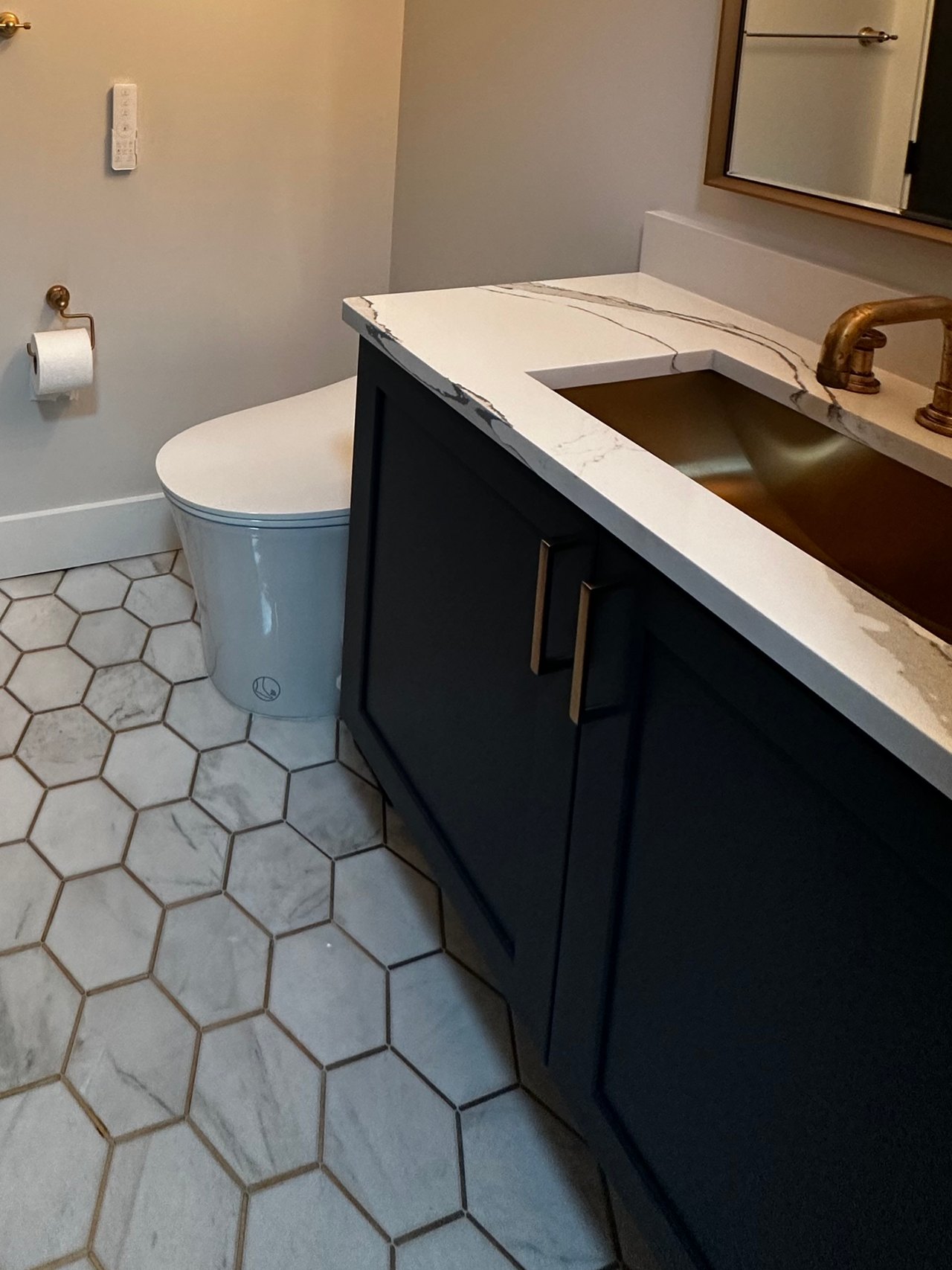 Powder room with a dark vanity, brass sink and fixtures, and white hexagonal floor tile