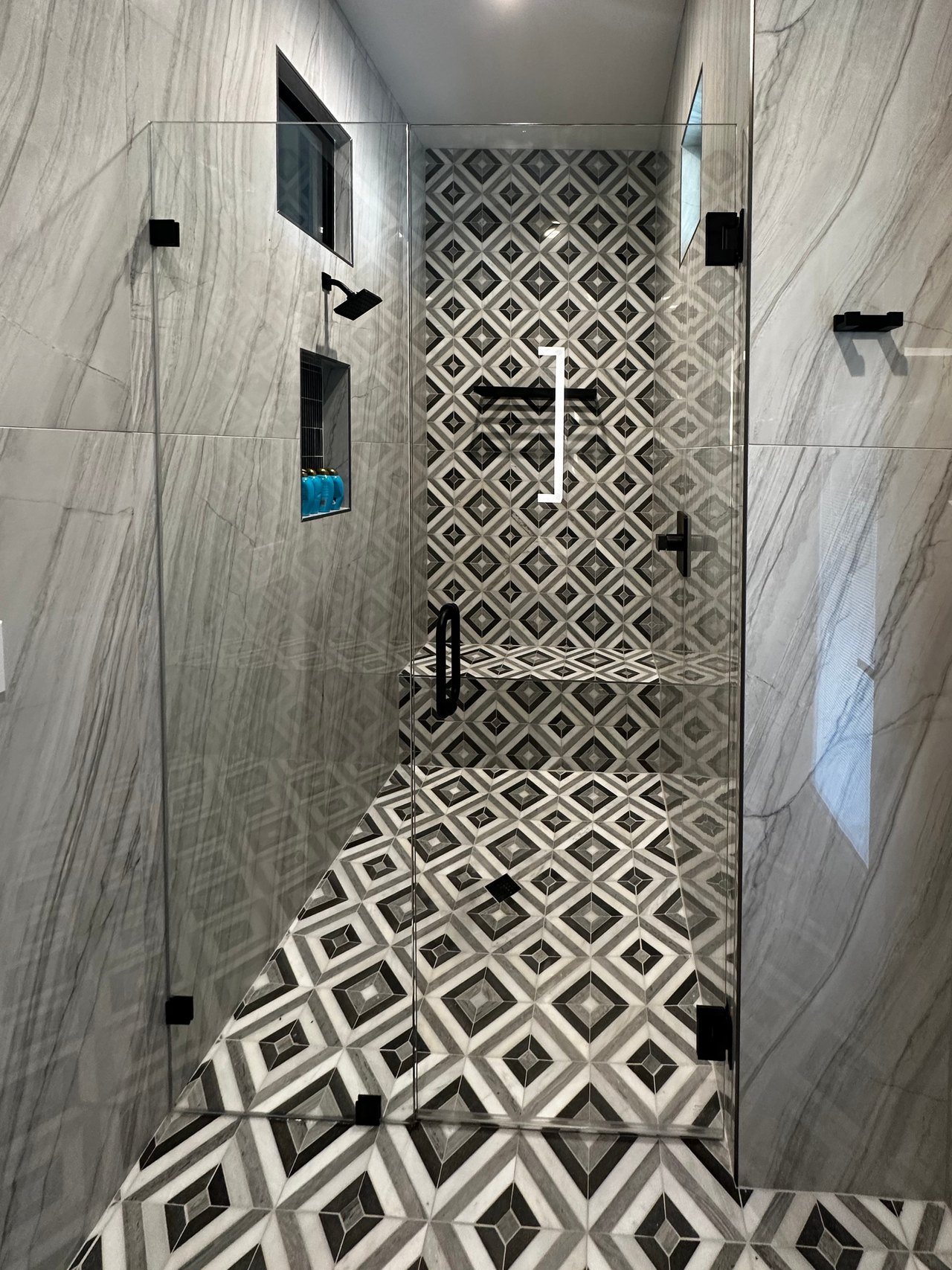 Glass shower with a geometric black-and-white tile wall, matching bench and floor, and black fixtures