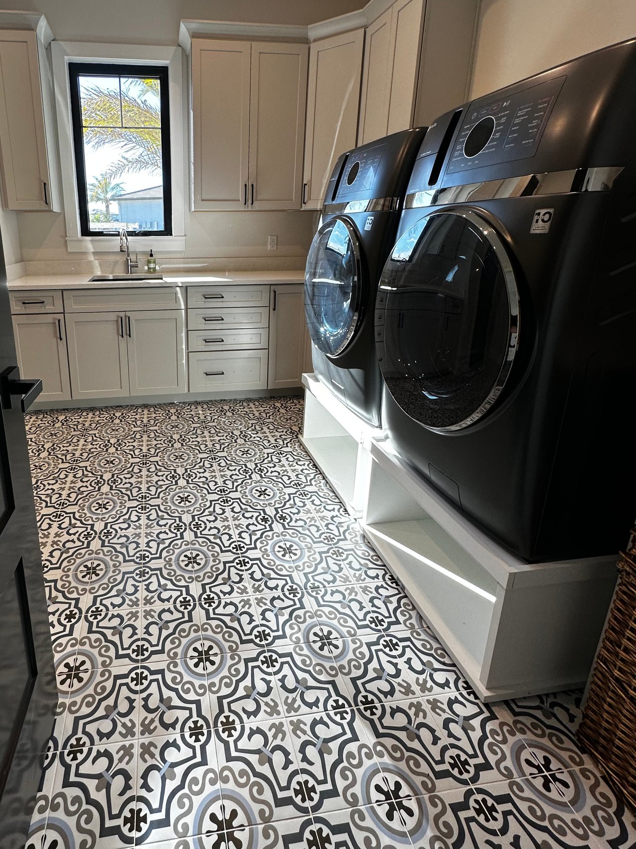 Laundry room with white cabinetry, a sink, raised front-loading appliances and patterned floor tile